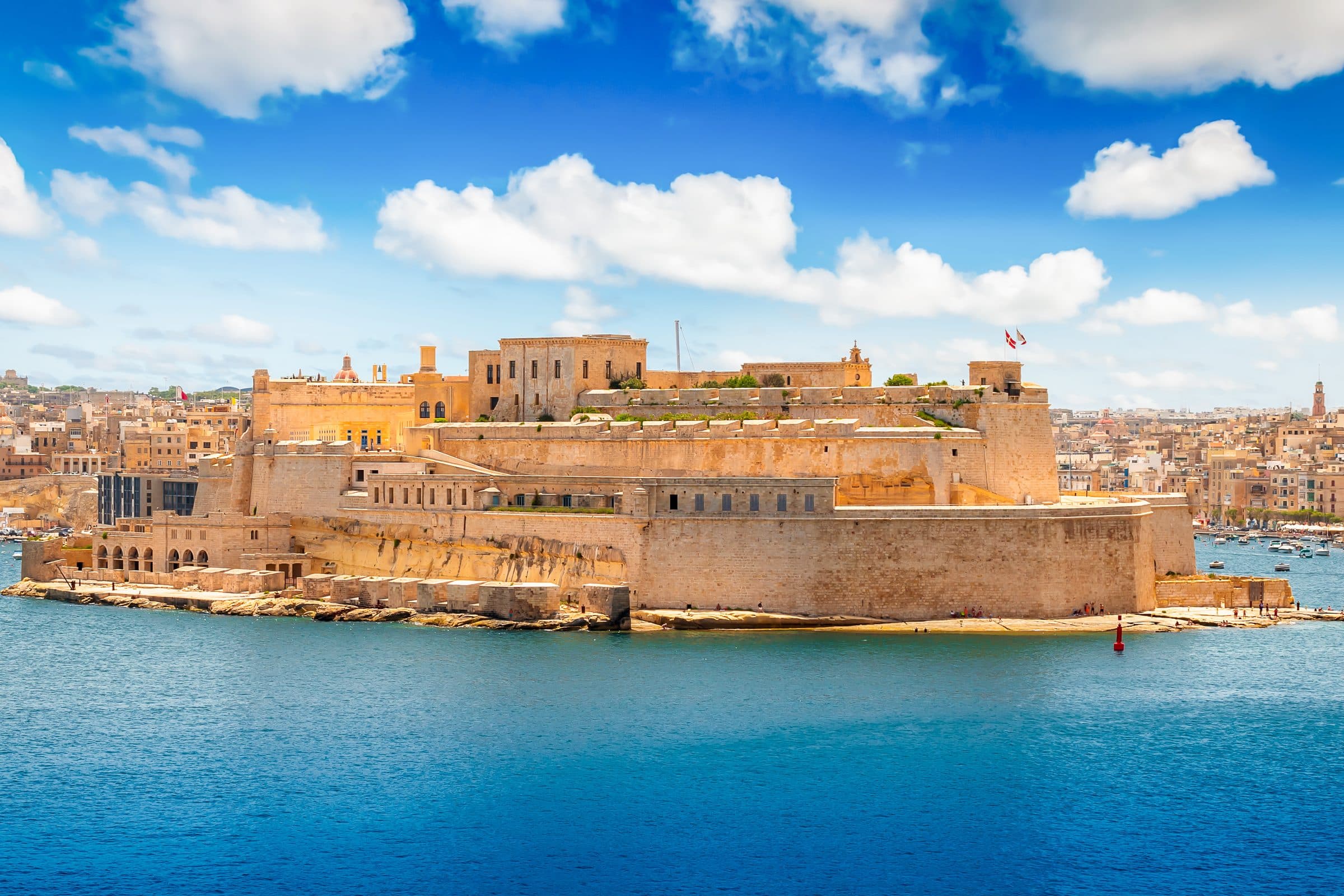 Fort St Angelo across the Grand Harbour in bright sunshine, its bastions reflected in deep blue water.