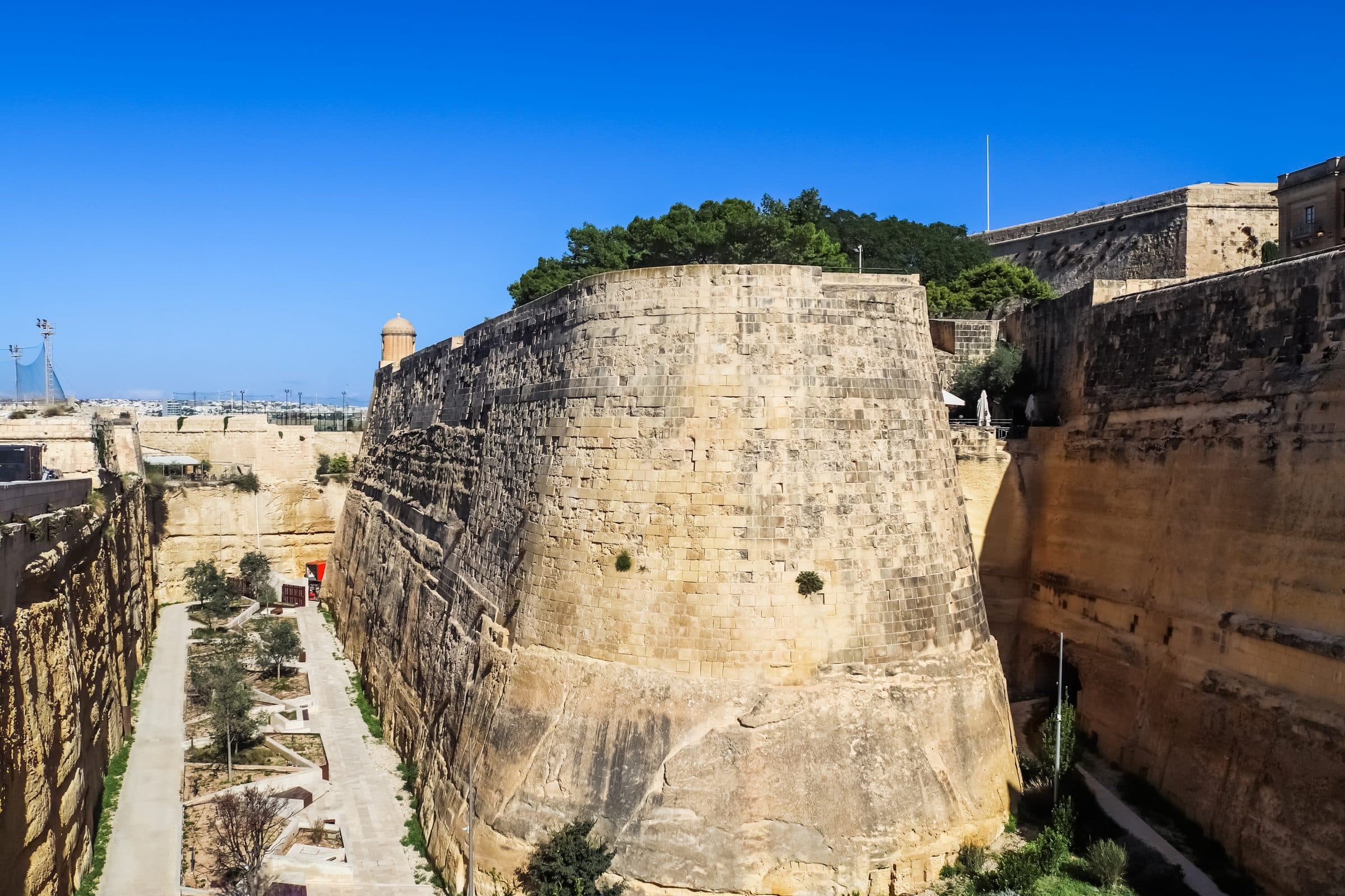 The honey-coloured bastion walls of Valletta's fortifications rising above the water against a deep blue sky.