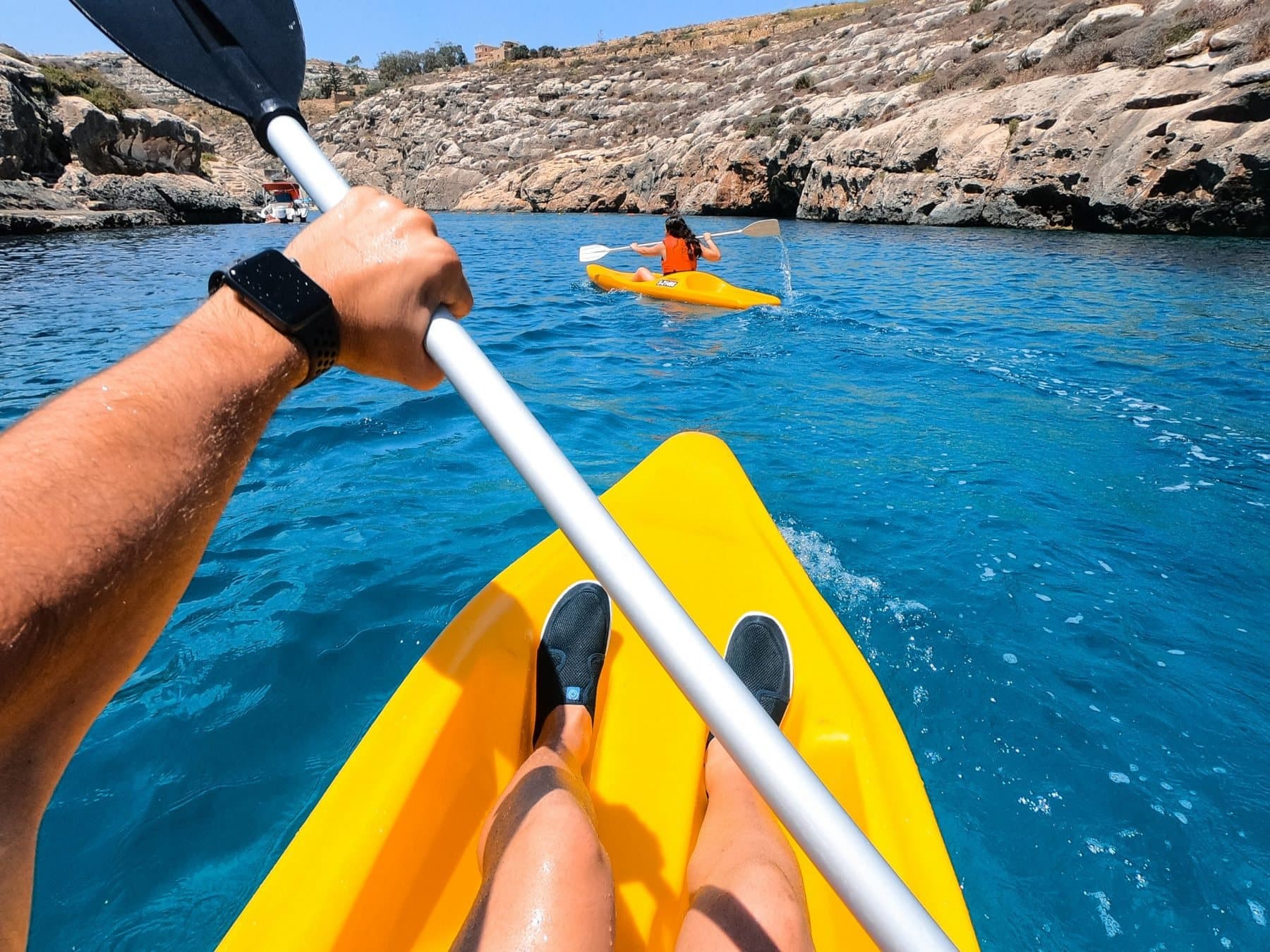 Kayaking across deep blue water in a rocky Maltese bay.