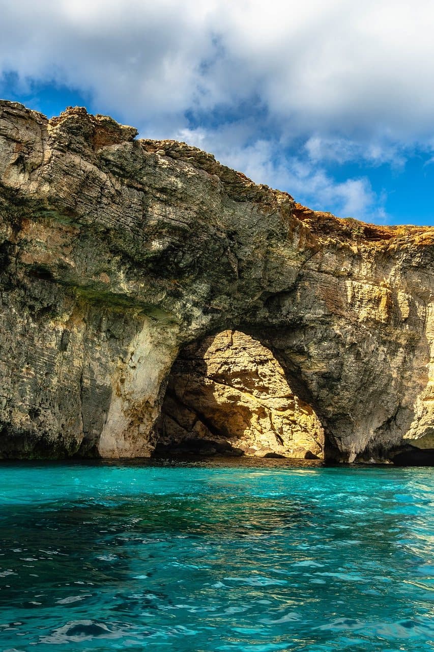 A natural sea arch off Comino, its limestone span framing bright blue sky above turquoise water.